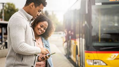 Two people stand in front of a Postbus looking at a smartphone.