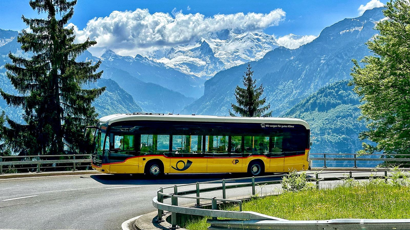 Electric Postbus on a bend with mountain panorama in the background