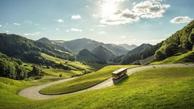 Le car postal descend le Passwang. Le paysage vert et vallonné est visible en arrière-plan.