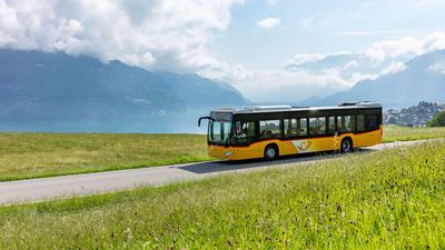 Fahrendes Postauto mit Thunersee im Hintergrund