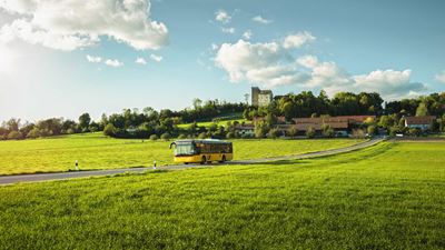 Postauto mit Dorf Habsburg und Schloss Habsburg im Hintergrund. © Michel Jaussi