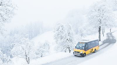 A small Postbus driving through the snowy streets of Sternenberg