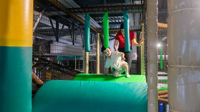 A young boy and a woman crawl over climbing modules in Kiddy Park Bülach.