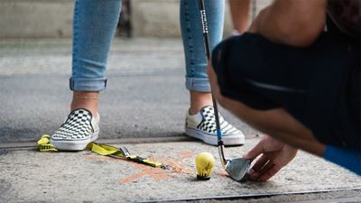 Nahaufnahme von Füssen und Beinen mit gelbem Ball und Schläger auf dem Urban Golf Parcours in Winterthur.