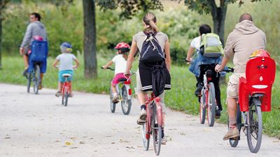Des adultes et des enfants font du vélo sur le circuit bordé d’arbres verts autour de l’aéroport de Zurich.