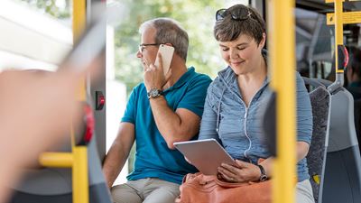 A woman reads on a tablet in a Postbus. Your neighbour is on the phone.