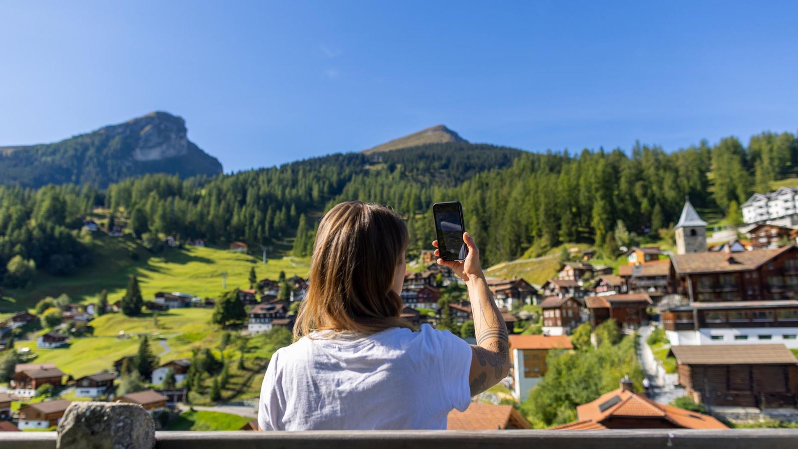 Übernachtungsgast fotografiert mit dem Smartphone eine Schweizer Berglandschaft – unterwegs mit der Gästekarte.