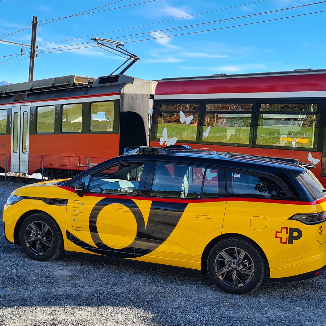 AmiGo vehicle is standing next to a train on a rural railway line.
