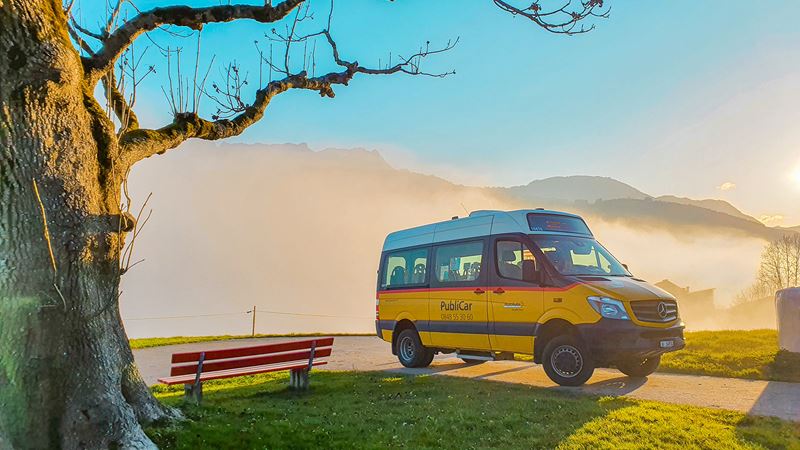 Au sommet d’une colline, un minibus CarPostal portant l’inscription PubliCar. 