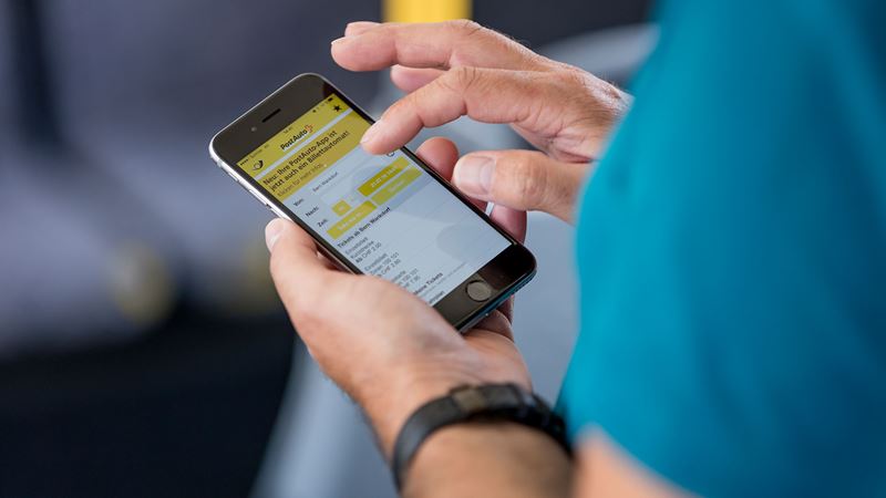 Nahaufnahme einer Hand welche die PostAuto App bedient. 