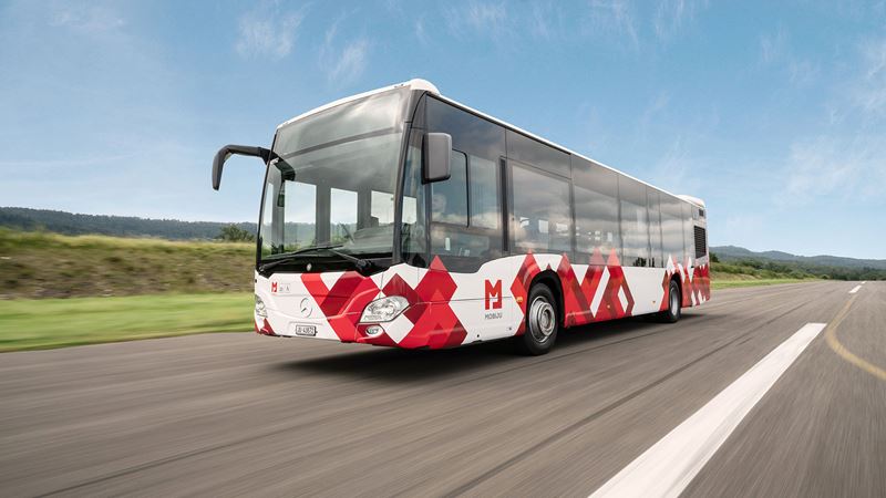 Ein Bus auf der Strasse im Jura im rot-weissen Mobiju Design. 