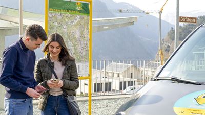 Two young people stand in front of a PubliCar looking at their smartphone.